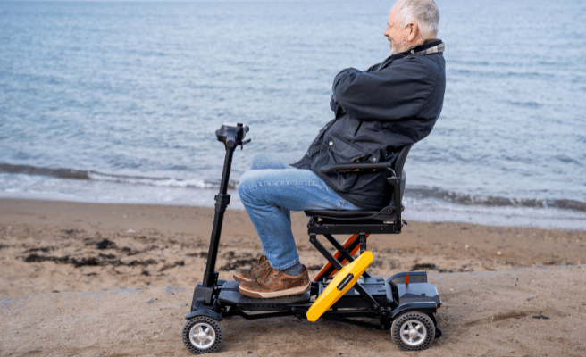 Orange, automatic folding Phantom mobility scooter used on hard sand | Phantom by Etech Mobility